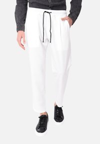 Pantaloni da jogging bianchi con vita elasticizzata e lacci neri, dotati di tasche laterali e una vestibilità rilassata. Abbinati a sneakers nere.
