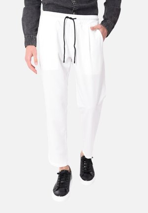 Pantaloni da jogging bianchi con vita elasticizzata e lacci neri, dotati di tasche laterali e una vestibilità rilassata. Abbinati a sneakers nere.