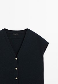 Top en maille noir sans manches avec col en V et trois boutons dorés décoratifs sur le devant.