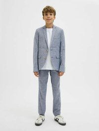 Világoskék szövetből készült öltöny, egysoros zakóval, alatta fehér pólóval, és szürke sportcipővel. A zakón két arany gomb található.