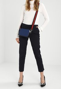 Černobílé pruhované zúžené kalhoty, kombinované s bílým rolákem a malou modrou kabelkou s červenými popruhy a černými akcenty.