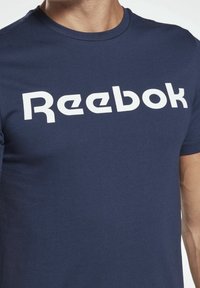 Granatowy t-shirt z krótkim rękawem, wykonany z bawełny, z wyraźnym białym logo Reebok na piersi. Gładka faktura, standardowy okrągły dekolt.