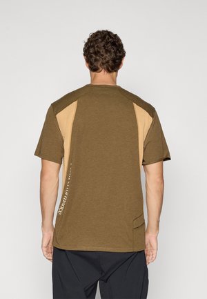 Brown short-sleeve t-shirt with light brown side panels and a slight curved hem. Features text detailing along one side and a relaxed fit.