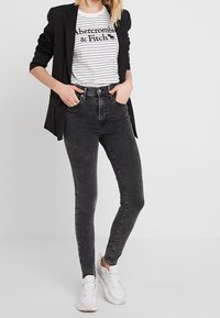 Jeans skinny neri a vita alta, abbinati a una maglietta a righe bianca e nera e a un blazer nero. Le sneakers bianche completano il look.
