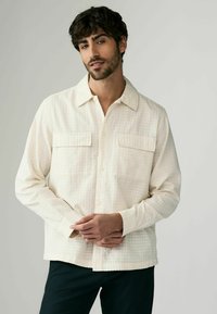 Beige button-up shirt with a textured grid pattern, featuring two chest pockets and a classic collar. Slim fit with long sleeves.