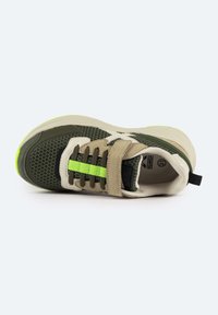 Zapatilla verde y beige que presenta materiales de malla y tela, con una suela texturizada y una franja de acento verde brillante. Incluye una correa ajustable.