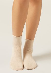 Beige Knöchelsocken aus weichem, strukturiertem Stoff mit einem gerippten Bündchen, das sich eng um den Knöchel schmiegt, mit einer abgerundeten Zehenpartie.