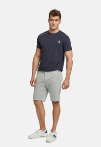 Navy cotton t-shirt with short sleeves and a crew neck, paired with light grey cotton shorts. White sneakers with navy and red accents.