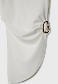 Tissu blanc drapé avec une texture lisse, mettant en avant un accent en métal doré unique sur le côté, créant un effet froncé.