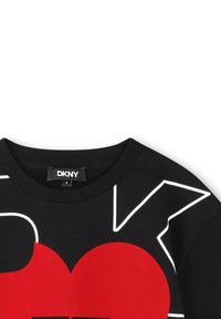 Camiseta negra con cuello redondo que presenta un gran gráfico de corazón rojo y formas con contorno blanco. Etiqueta de la marca "DKNY" visible en el cuello.