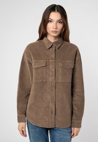 Bruine corduroy overhemd met een knoopsluiting kraag, twee borstzakken en een relaxte pasvorm. Beschikt over een gestructureerd oppervlak en stevige knopen.