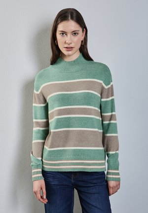 Gestreifter Strickpullover in Mintgrün, Beige und Weiß, mit hohem geripptem Kragen und gerippten Bündchen, kombiniert mit blauen Jeans.
