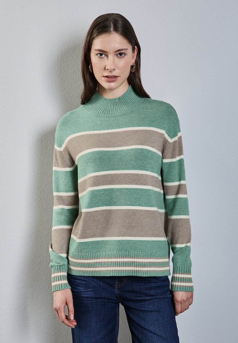 Maglione a righe in verde menta, beige e bianco, con colletto alto a coste e polsini a coste, abbinato a jeans blu.