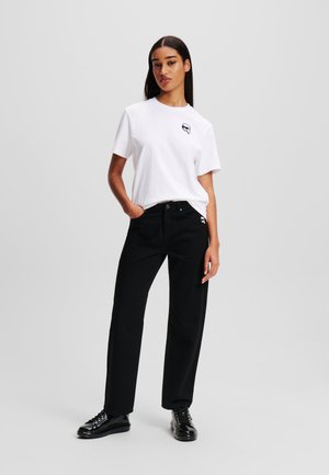 White short-sleeve t-shirt with a black graphic on the chest, paired with high-waisted black straight-leg trousers and black sneakers.