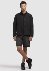Black lightweight jacket with a high collar, zip closure, paired with dark shorts and black high-top sneakers. Simple, modern design.