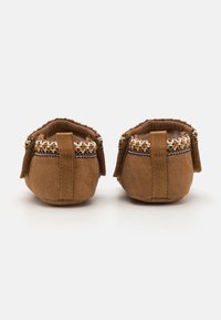 Brune semskede tumlingesko med en teksturert overflate, dekorative vevde detaljer og bakre stropp for enkel påkledning. Mykt indre fôr.