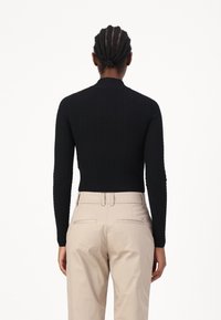 Top negro de manga larga de canalé con cuello alto, combinado con pantalones beiges que tienen bolsillos traseros y una cintura ajustada.