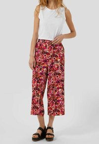 Pantalon à jambes larges à motif floral dans des tons de rose et d'orange, avec une taille haute et un tissu lisse. Associé à un haut blanc sans manches.