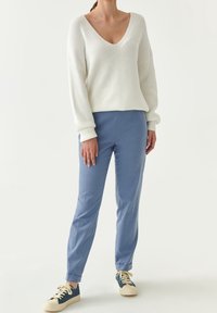 Witte geribbelde trui met V-hals, gecombineerd met lichtblauwe op maat gemaakte broek en blauwe sneakers met crèmekleurige veters en zolen.
