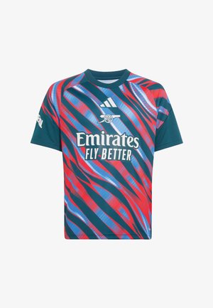 Niño sosteniendo un balón de fútbol rojo del Arsenal, vistiendo una camiseta del Arsenal con el logo de Emirates Fly Better y pantalones cortos blancos con ribete rojo.