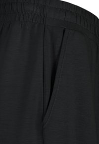 Schwarze Jogginghosen sind mit einem elastischen Bund, seitlichen Taschen und einem glatten, strukturierten Stoff mit dezentem Glanz ausgestattet.
