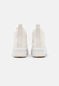 Pár bílých vysokých tenisek Converse All Star s fleece texturou, viditelnými poutky na patě a značkovými gumovými podrážkami zobrazenými zezadu.