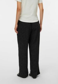 Črne širokorepe hlače iz mešanice volne z teksturiranim zaključkom, z razpoloženim krojem, ravnim pasom in žepi, nošene s svetlim zgornjim delom.