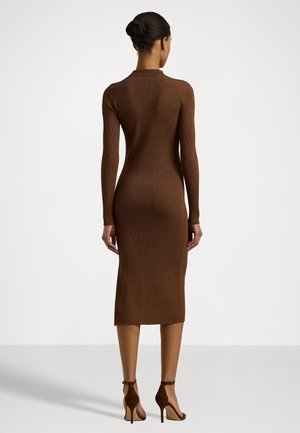Woman wearing a fitted, long-sleeve, ribbed brown midi dress and brown high-heeled sandals, shown from the back against a plain background.