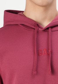 Maroon pullover hoodie made from soft fabric, featuring a drawstring hood and embroidered "GAP" logo in a matching shade.