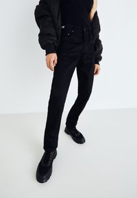 Jeans neri realizzati in denim, caratterizzati da una vestibilità slim, design a cinque tasche e scarpe nere abbinate con suole testurizzate. Accentuati da un giubbotto imbottito.