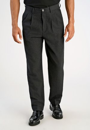 Dunkelgraue Wollhose mit gefaltetem Design, flachem Bund und einem einzigen Knopfverschluss. Gepflegte schwarze Schuhe runden den Look ab.