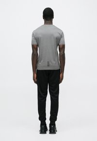 Pelēka īsroku krekls uz cilvēka, valkājot melnas sporta bikses un apavus. Krekla aizmugurē ir horizontāla svītru detaļa.