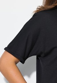 Černá krátkosrstá košile z měkké tkaniny, s ohrnutými rukávy a volným střihem. Textura vypadá hladce se subtilními linkami.