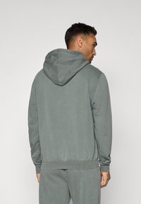 Szürke kapucnis pulóver puha textúrával, bordás mandzsettákkal és aljjal, lazább szabással. Minimalista dizájn, látható minták vagy logók nélkül.