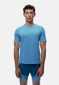 Šviesiai mėlyna trumpomis rankovėmis sportinė marškinėliai su apvaliu kaklu, pagaminti iš lygaus audinio. Pavaizduoti su tamsiai mėlynomis sportinėmis šortais, minimalizmo dizainu.