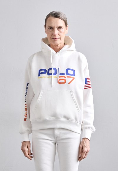 Fehér kapucnis pulóver, amelyen kék és narancssárga szöveggel olvasható a "POLO 67" felirat. A kézen kék színnel szerepel a "RALPH LAUREN" felirat, valamint egy kis amerikai zászló díszítés.