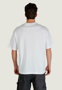 Biały bawełniany t-shirt o luźnym kroju, krótkich rękawach i okrągłym dekolcie, widoczny od tyłu. Materiał wydaje się gładki i miękki.