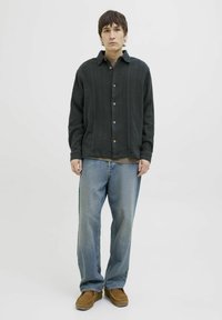 Donkergroene overhemdsblouse met textuurstof, gecombineerd met lichtblauwe rechte jeans en bruine suède schoenen. Eenvoudig ontwerp en relaxte pasvorm.