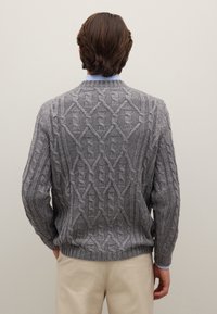 Grauer Strickpullover mit einer strukturierten Zopfmuster-Optik, gerippten Bündchen und Saum sowie einem Rundhalsausschnitt, kombiniert mit hellen Hosen.