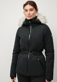 Sort isoleret jakke med pelsforet hætte, bæltestrop i taljen og lynlåslommer. Glat tekstur med et strømlinet, tætsiddende design.