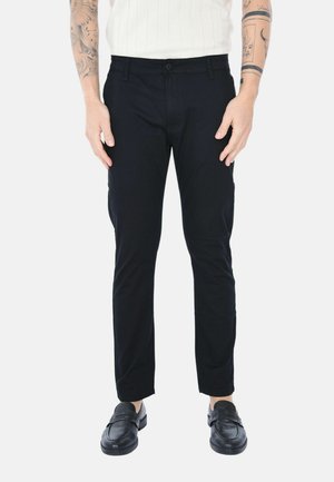 Pantaloni neri slim-fit con una texture liscia, dotati di chiusura con bottone e tasche frontali. Indossati con mocassini neri.