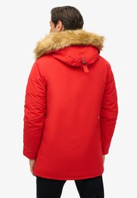 Czerwona pikowana parka z kapturem podszytym sztucznym futrem, regulowanymi paskami i gładką fakturą, o długości do kolan.
