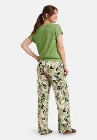 Groen textuur t-shirt met korte mouwen en een ronde rug, gecombineerd met wijdvallende broeken met bloemenprint in groene, zwarte en beige tinten.
