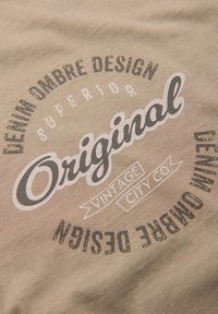 Béžová látka s potištěným grafickým vzorem a textovými prvky v černé a bílé barvě, včetně "Originál," "Vintage City Co.," a geometrických tvarů.