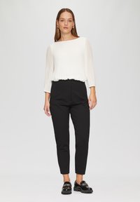 Wit, geplooid blouse met een geraffineerde taille, gecombineerd met zwarte, tapse broeken en glanzende zwarte instappers, tegen een neutrale achtergrond.