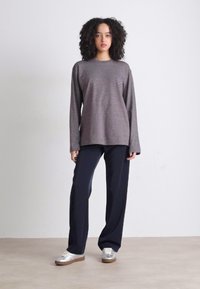 Langermet stripet topp i grå og marsala kombinert med mørk marineblå vide bukser. Modellen har på seg sølvfargede sneakers, som viser en uformell stil.