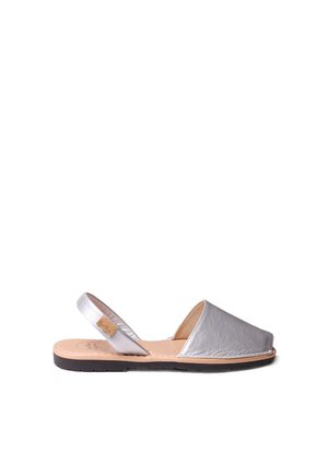 Sandale en cuir argenté à talon ouvert avec un bout arrondi et des détails cousus. Présente une semelle plate noire et une semelle intérieure beige.