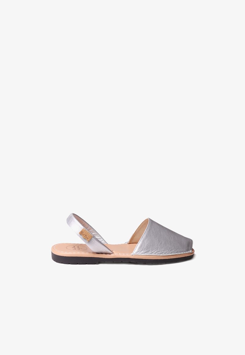 Hopeasävyinen nahkainen slingback-sandaali, jossa on pyöristetty kärki, avoin kanta ja ommeltu koristelu. Varustettu litteällä mustalla pohjalla ja vaaleanruskealla pohjallisella.