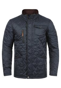 Marineblå quiltet jakke med høj krave, der har en lynlås-lomme og to frontlommer, lavet af glat, tekstureret stof.