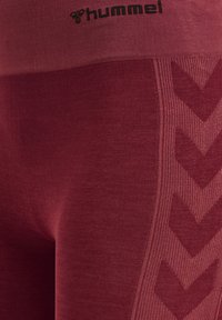 Leggings bordeaux caratterizzati da un tessuto a coste testurizzato, un ampio elastico in vita e un distintivo motivo a zigzag lungo il lato in una tonalità leggermente più scura.